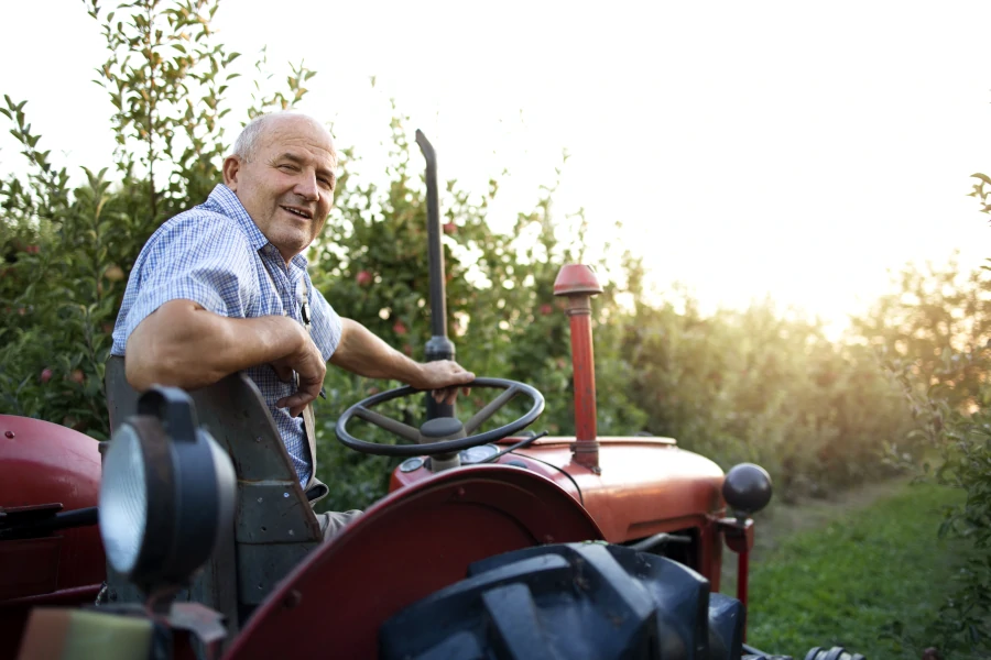 Mężczyzna, rolnik na traktorze w sadzie owocowym